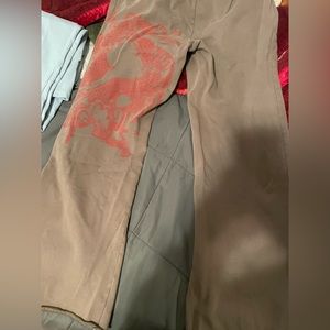 Low rise pants that are brown with a red dragon on the left leg.